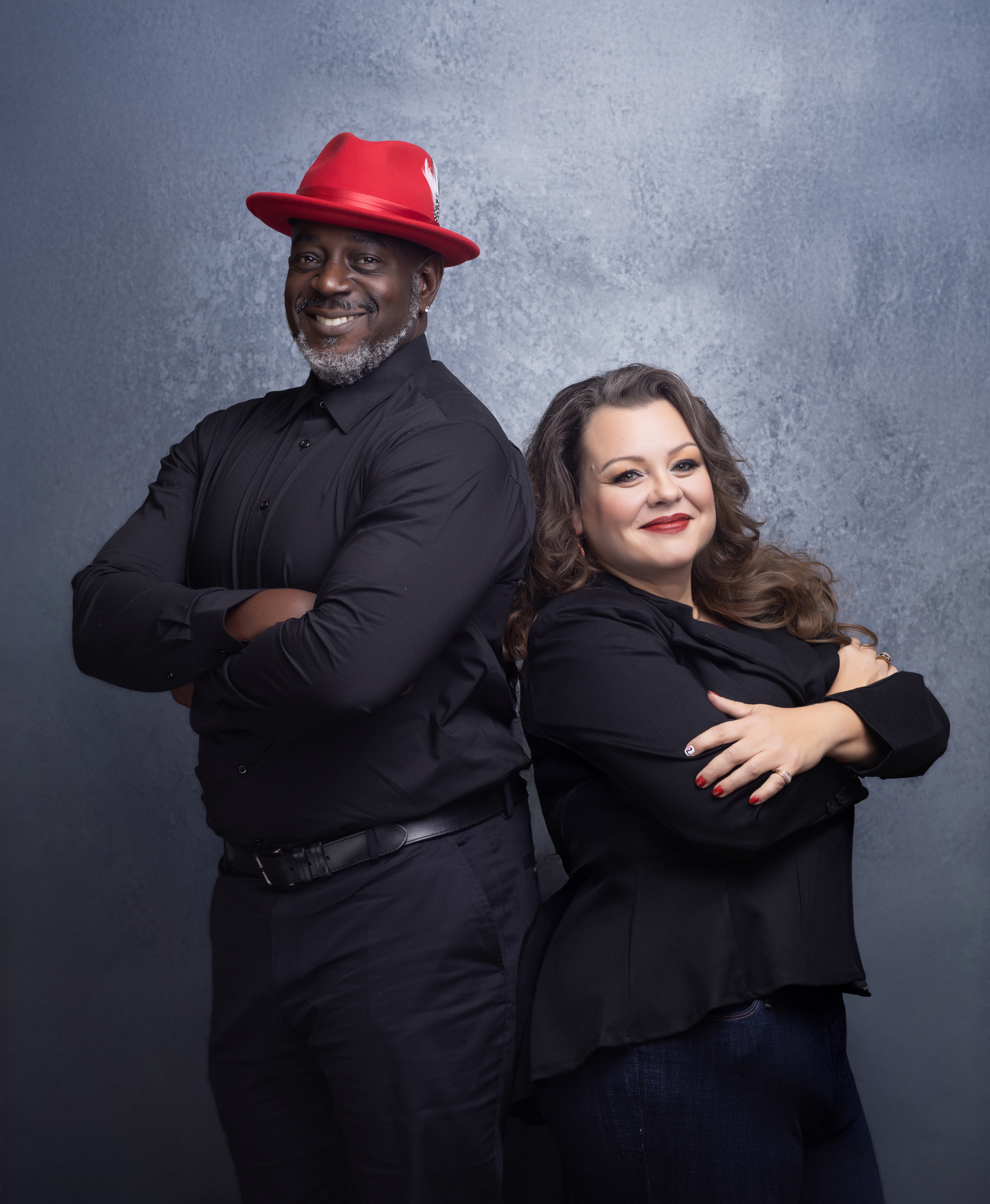 Business power couple stands back to back with their arms crossed and smiles on their faces.